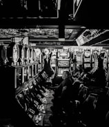 A dimly lit casino filled with rows of slot machines, some occupied by people. The machines' lights contrast with the dark surroundings, creating a vibrant yet subdued atmosphere.